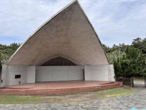 
An outdoor amphitheater with a large, curved concrete roof is shown. 