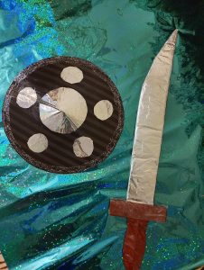 A toy sword and shield, hand made, on sparkly paper.