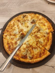 A freshly baked pizza on a wooden serving board, topped with melted cheese and mushrooms. 