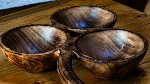 A close-up, high-angle photograph of a rustic, three-section serving bowl hand-carved from dark, polished wood with a prominent natural grain.