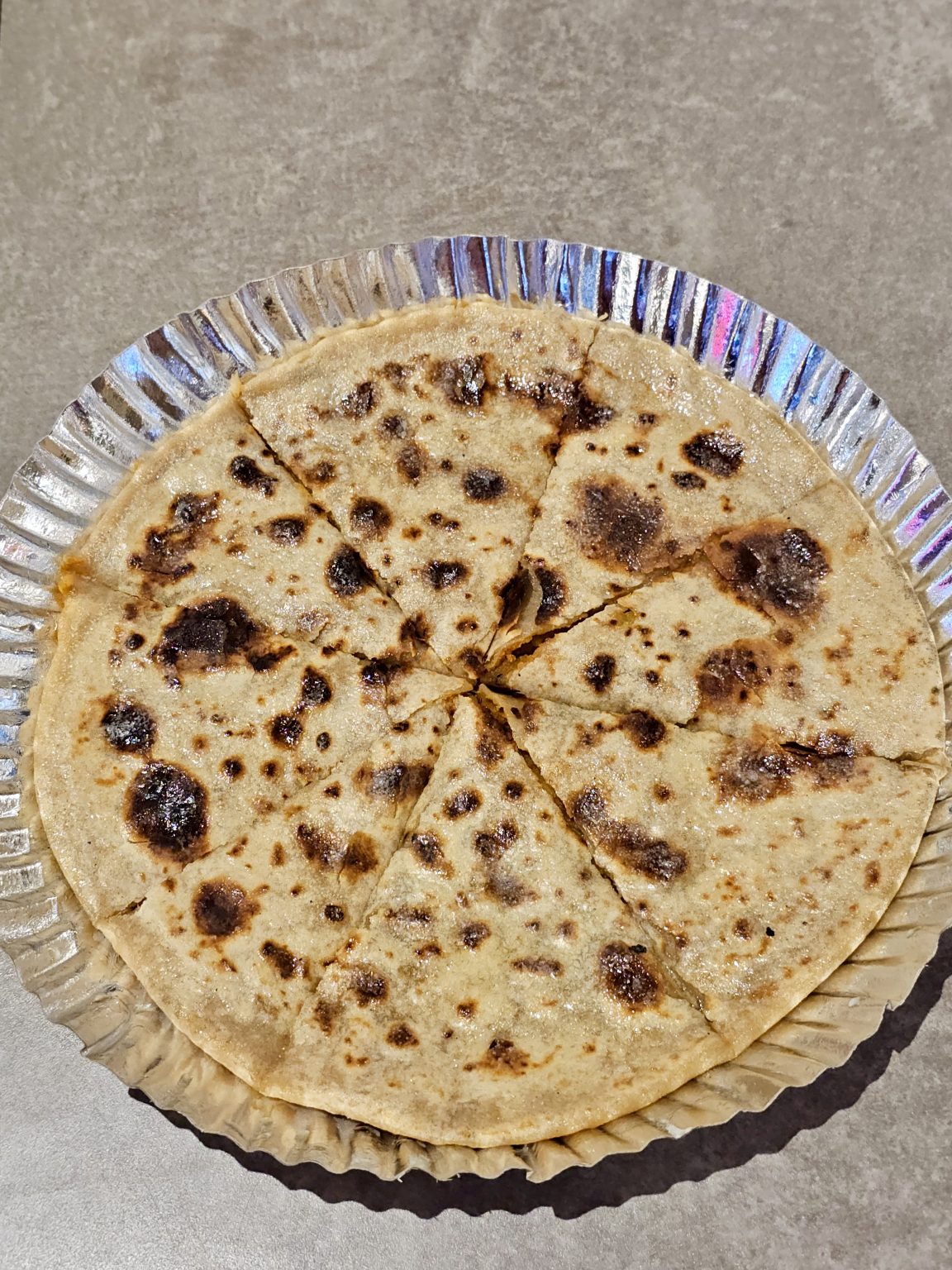 A freshly made Aloo (potato) paratha, cut into slices, served on a foil plate at Bandra, Mumbai. The golden brown spots and simple presentation make it look warm and ready to eat.