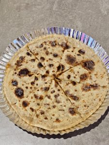A freshly made Aloo (potato) paratha, cut into slices, served on a foil plate at Bandra, Mumbai. The golden brown spots and simple presentation make it look warm and ready to eat.
