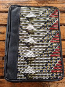 A laptop sleeve with a colorful geometric fabric pattern and black side panel, placed on a slatted wooden surface.
