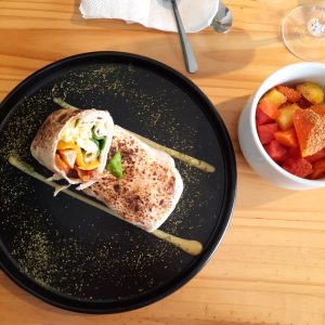 Breakfast wrap cut in half on a plate, decorated with sauce and fruit on the side.