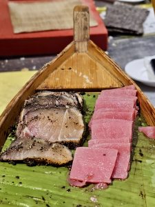 Slices of fresh sashimi served on a bed of green leaves on a wooden tray. A clean and simple presentation captured in Worli, Mumbai.