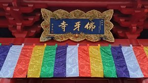 Ornate temple sign with gold Chinese characters and dragon carvings above a row of multicolored hanging banners.