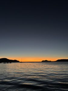 A calm ocean bay at dusk with a deep blue sky fading into a glowing orange horizon.