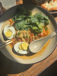 
A bowl of noodles topped with sliced boiled eggs, cooked vegetables including bok choy and carrots, and garnished with chopped green onions.