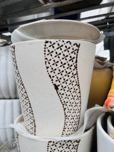 A close-up of a textured white decorative pot with curved design and brown lace-like detailing.