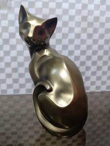 Golden cat sculpture sitting with its tail curled, looking back in an abstract style.