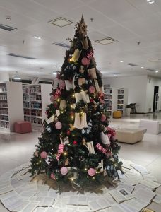 A unique Christmas tree decorated with books, lights, and ornaments inside a modern library, creating a warm and festive atmosphere