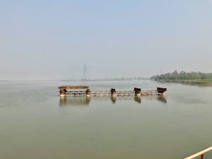 A calm river with a partially built, weathered bridge in a hazy setting.