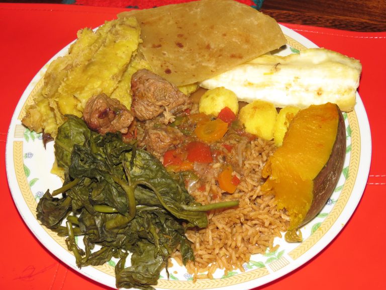 A colorful Ugandan meal with stewed beef, pilau, pumpkin, matooke, cassava, chapati, and green vegetables.