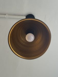 Close-up of a round ceiling light fixture with a spiraled gold interior and a central white bulb, creating a warm and modern ambiance.