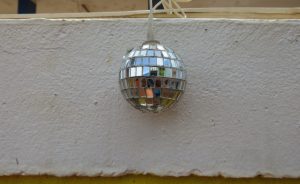 
A small disco ball hangs against a textured white wall, reflecting light and colors from its surroundings.