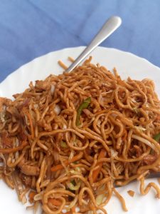 A plate of stir-fried noodles with meat and vegetables, with a fork on a blue background.