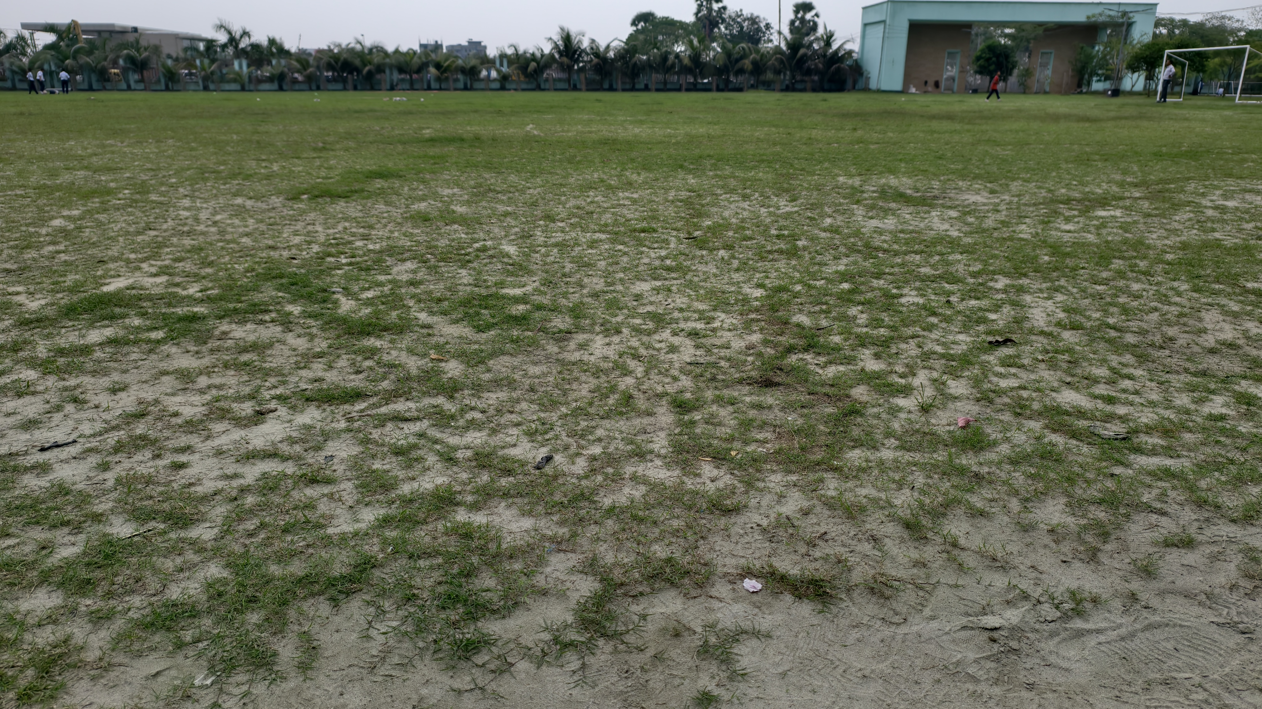 A wide view of a large open field with patches of green grass and sand under a cloudy sky.