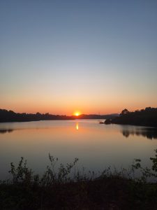 A serene landscape featuring a calm body of water reflecting the colors of a setting sun.