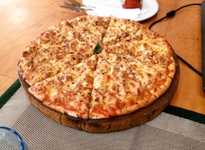 A thick crust meat lovers pizza with melted cheese and ground meat, sliced into eight and served on a wooden board, topped with a basil leaf on a light wooden table.