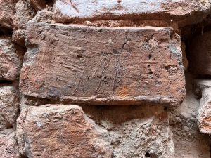Close-up of an old weathered brick wall with a prominent rectangular brick showing scratches and markings.