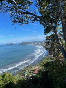 A scenic view of a coastline featuring a curving beach with gentle waves lapping at the shore.