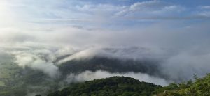 View from Cerro El Caballito with green hills and a sea of clouds under a blue morning sky.