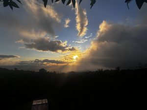A stunning sunset scene over a landscape, featuring a vibrant orange sun setting amidst dramatic clouds. 