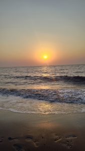 Golden sunset over the ocean with gentle waves rolling onto a sandy beach, reflecting warm orange light across the water and wet shore.
