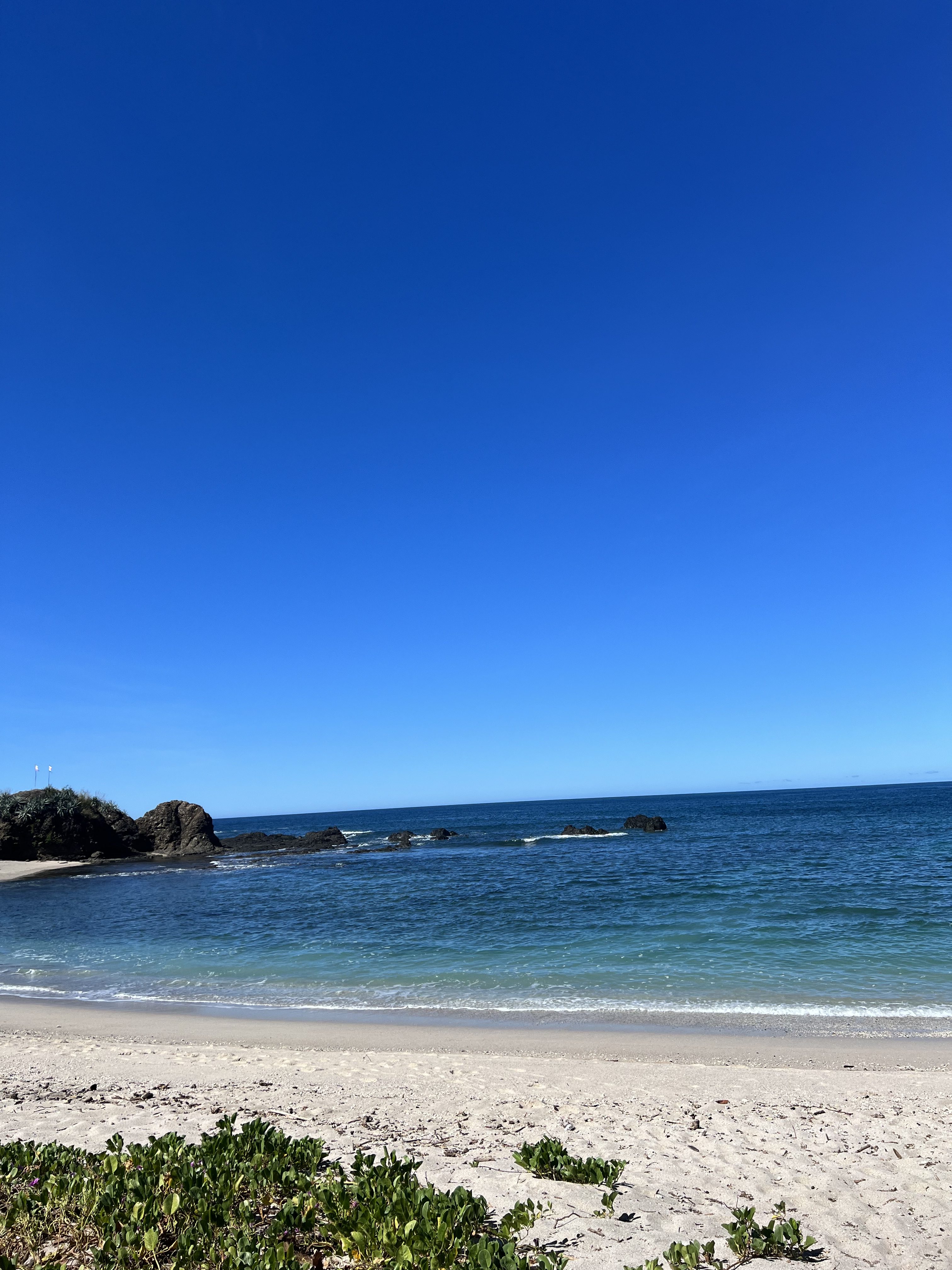 A calm beach with clear blue water, soft white sand, and a bright sky that creates a peaceful coastal view.