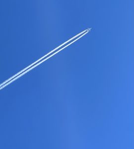 A commercial airplane gliding through a clear blue sky, leaving behind two white contrails that stretch towards the horizon.