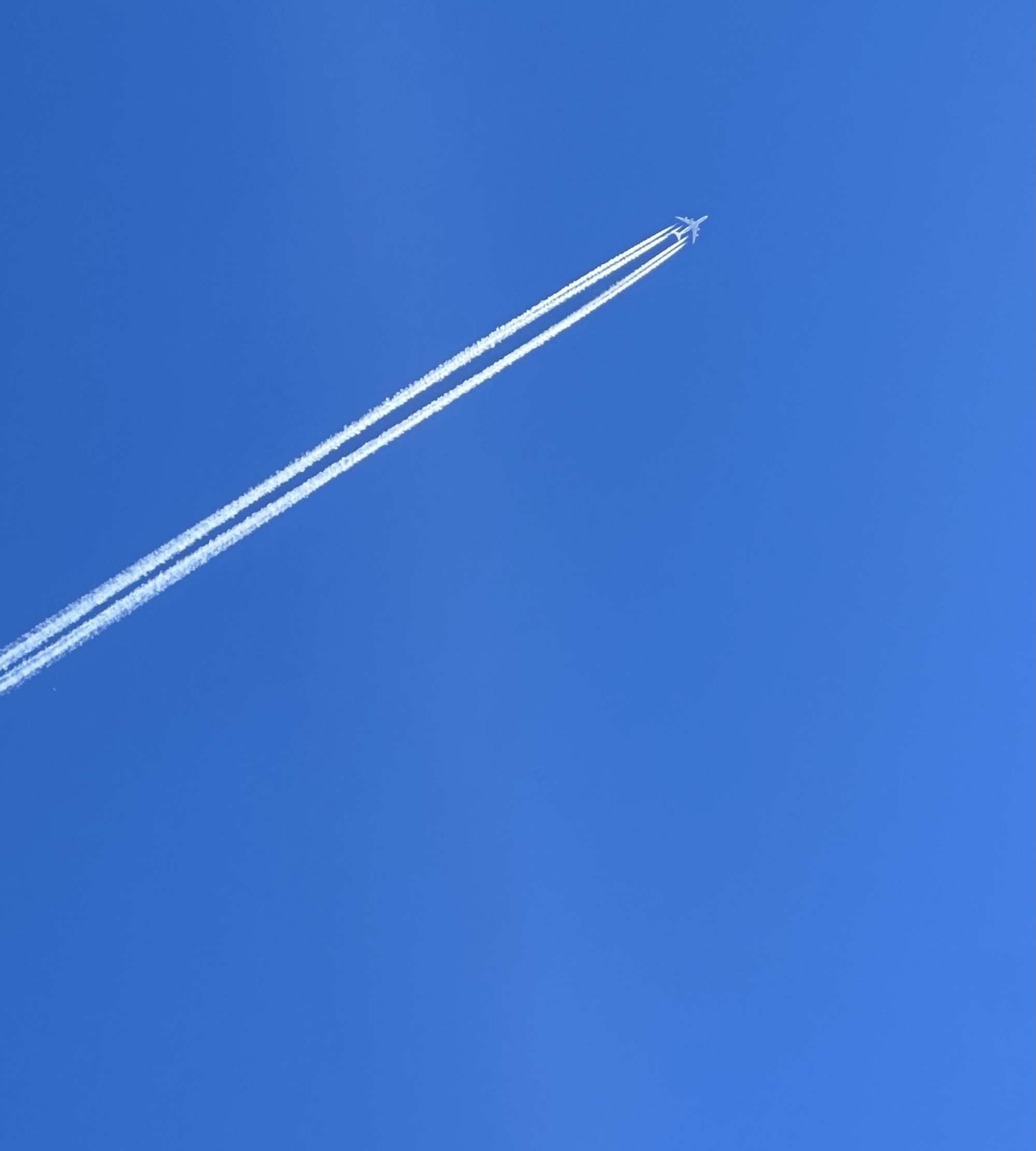 A commercial airplane gliding through a clear blue sky, leaving behind two white contrails that stretch towards the horizon.
