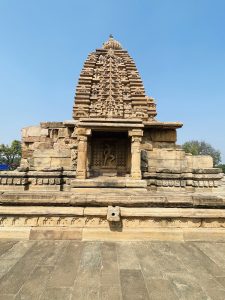 An ancient stone temple with detailed carvings stands under a clear blue sky. The symmetry and fine work show a rich heritage. Captured at Pattadakal, Bagalkot, Karnataka. 
