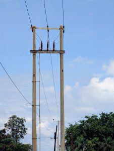
A tall concrete utility pole with multiple wires extending from it, set against a blue sky with scattered clouds.