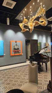 A refined interior space featuring a modern chandelier, a grand piano, and artistic decor. The composition highlights lighting, textures, and architectural details.