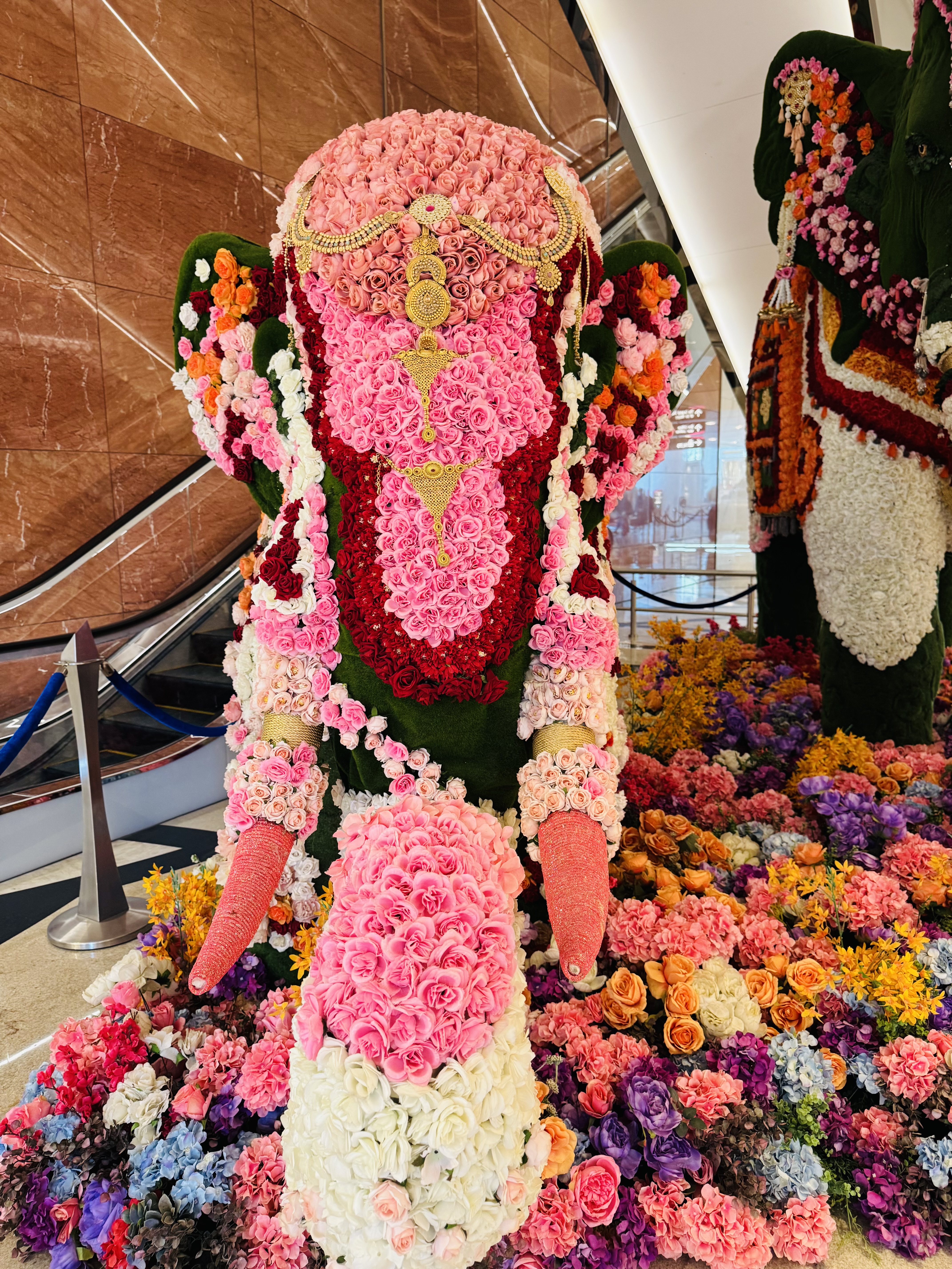 A large floral sculpture representing an elephant is adorned with vibrant shades of pink, red, and white flowers, creating a lavish and intricate design.