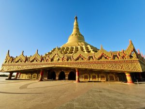 A wide view of the grand golden pagoda with detailed carvings under a clear blue sky at Global Vipassana Pagoda, Gorai Village, Mumbai. The open space adds a calm and peaceful feel. 
