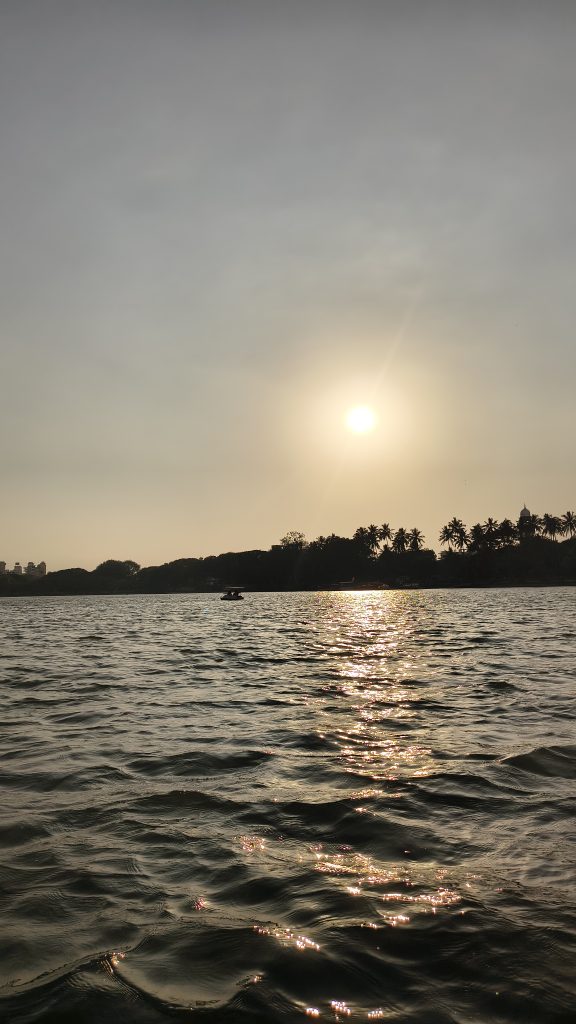 Sunset over a lake with golden light reflecting on rippling water. Silhouettes of trees and a small boat are visible against the evening sky.