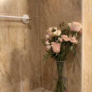 A bouquet of pink roses in a glass vase on marble tiles, beside a towel bar, in soft indoor light.