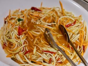 A bowl of noodle salad mixed with vegetables and sauce, with serving tongs placed on top. A casual food scene captured in Worli, Mumbai. 