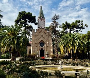 A historic church with a green pointed roof, surrounded by palm trees and greenery in Santiago, Chile.