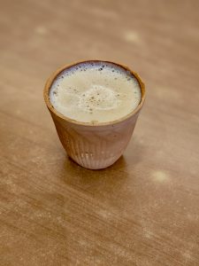 A small cup of hot coffee served in a clay kulhad (pot) in Kurla, Mumbai. The creamy foam on top and the simple wooden table create a warm, cozy street-style feel.