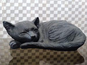A black sculpture of a sleeping cat, positioned curled up with its head resting on its forelegs.
