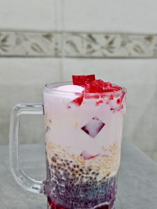 A glass of falooda with milk, basil seeds, vermicelli, and red jelly pieces at Bandra, Mumbai. The layers and colors make the drink look rich, refreshing, and delicious. 
