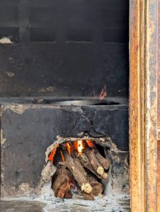 
A traditional stove with a visible fire burning at the base, surrounded by logs and ash.