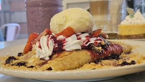 A plate of crepes topped with whipped cream, strawberries, and berry sauce, accompanied by a scoop of vanilla ice cream.