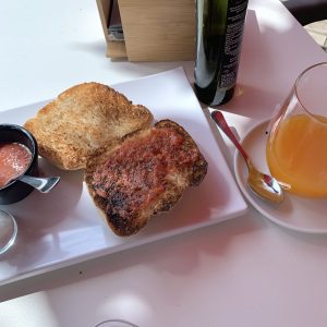 A traditional Spanish breakfast of toasted bread with tomato, served with orange juice and olive oil on a white table in bright morning light.