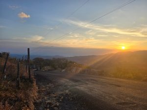 Sunset along a rural road with rays of sunlight stretching across the landscape, creating a warm and tranquil scene.