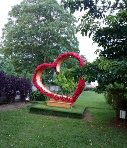 Wooden heart sculpture decorated with red flowers in a lush green garden.