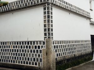 A corner of a building in Kurashiki City with smooth white walls and a lower section of glass bricks framed by black tiles.
