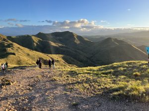 Group of people hiking on a mountain trail surrounded by green hills and natural scenery.